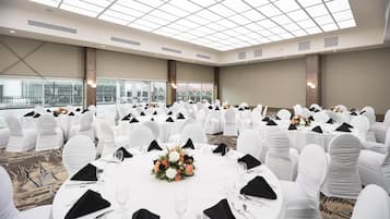 A banquet hall with round tables, white chairs, and a high ceiling with skylights.