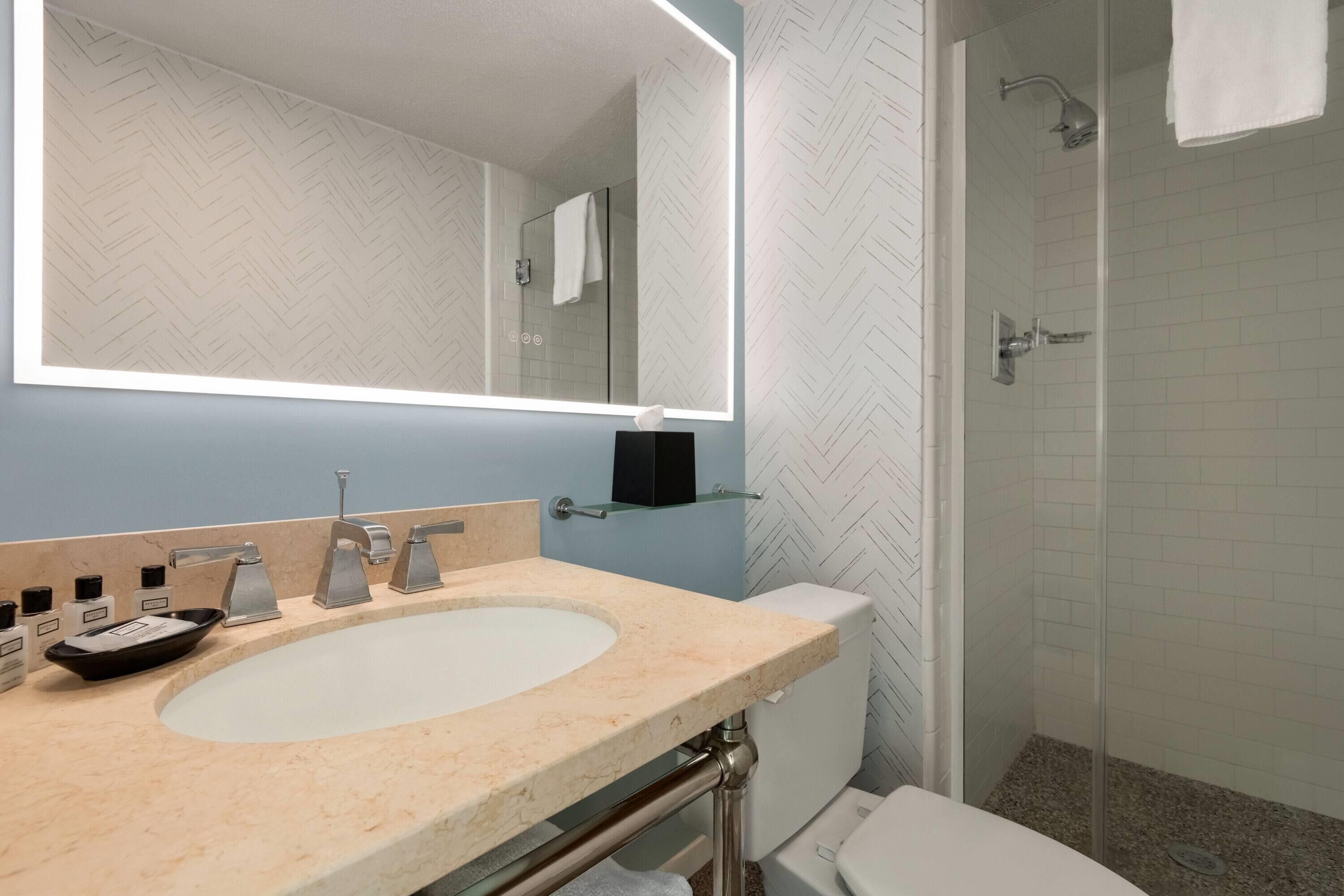 A bathroom with a white sink, a mirror, a glass shower enclosure, and a toilet.
