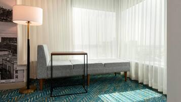 A room with a grey sofa, a small table, a floor lamp, and sheer curtains.