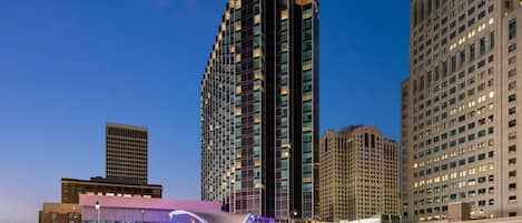 A modern hotel with a distinctive curved roof structure, surrounded by high-rise buildings.