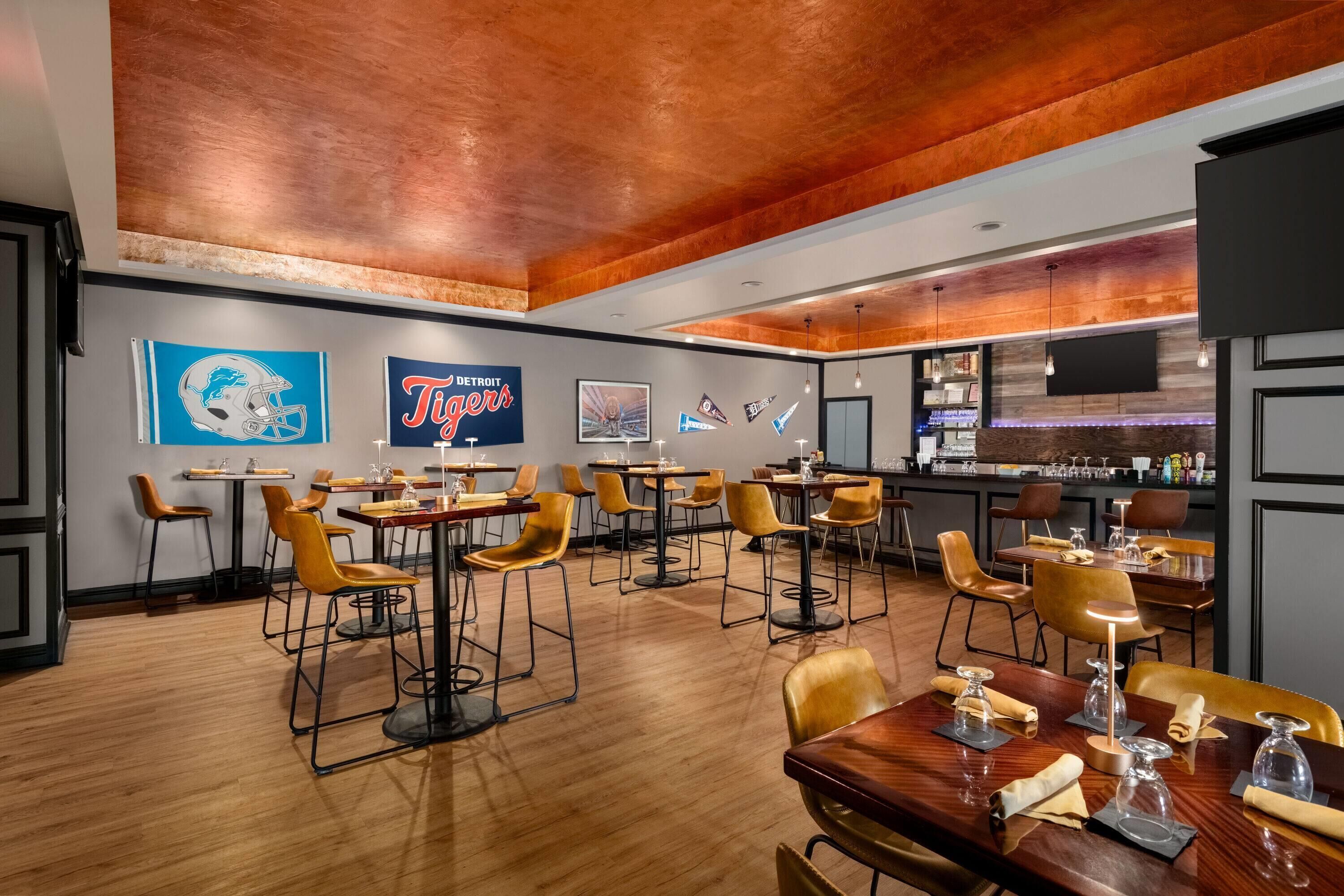 A restaurant with a modern interior, featuring wooden tables and chairs, a bar area, and sports memorabilia on the walls.