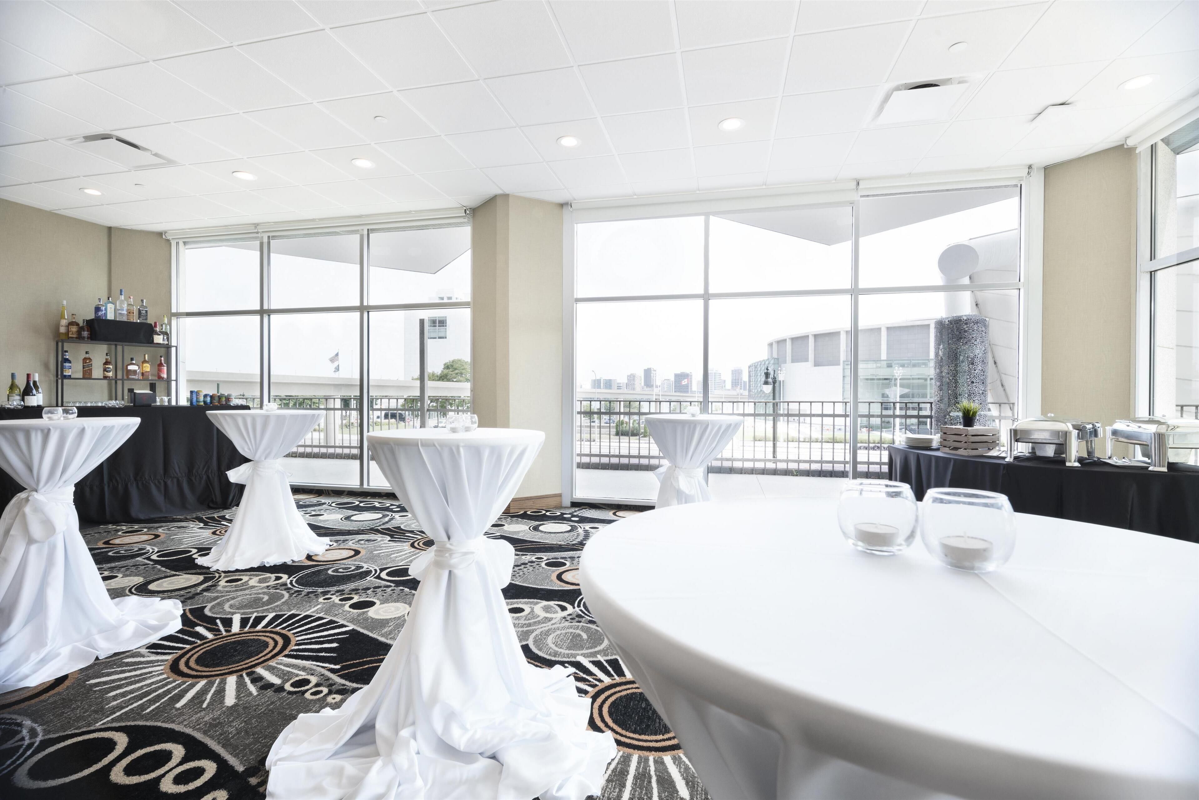 A conference room with round tables and chairs, large windows with a city view, and a carpeted floor.