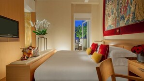 A modern hotel room with a large bed, a television, a small table with a plant, and a large tapestry on the wall. - Hotel Raphaël – Relais & Châteaux (Rome)