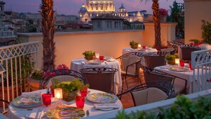 A rooftop terrace with tables set for dining, palm trees, and a view of a large dome building in the background. - Hotel Raphaël – Relais & Châteaux (Rome)
