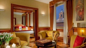 A luxurious hotel room with a large bed, a sitting area with a chessboard, a view of a building through a window, and a painting on the wall. - Hotel Raphaël – Relais & Châteaux (Rome)