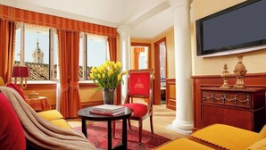 A hotel room with a large window, a red armchair, a table with a book, and a television on the wall. - Hotel Raphaël – Relais & Châteaux (Rome)
