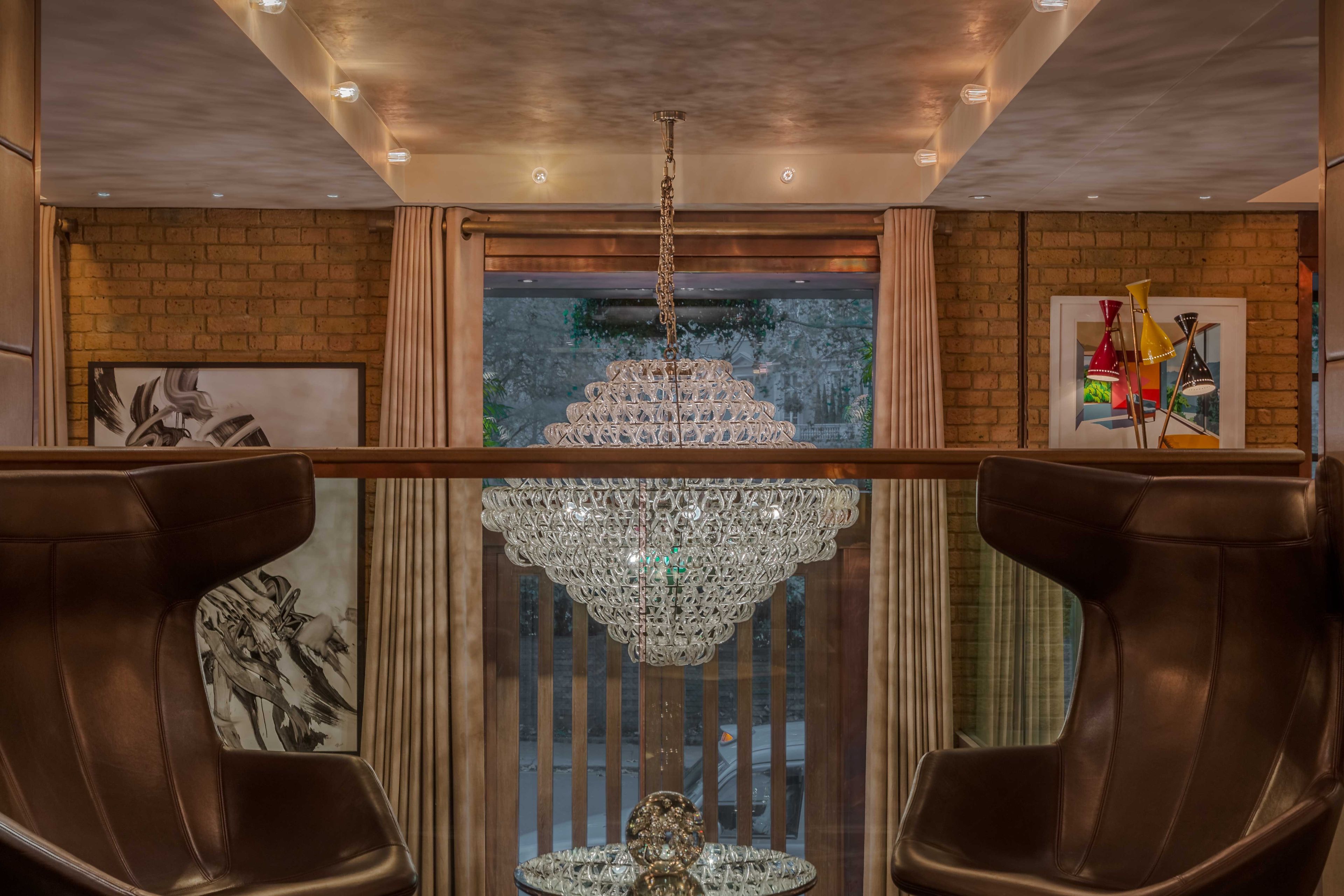 A room with a chandelier, leather chairs, a brick wall, and a window with blinds.