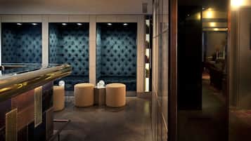 A modern bar area with a dark blue upholstered wall, a polished bar counter, and three round seating stools.