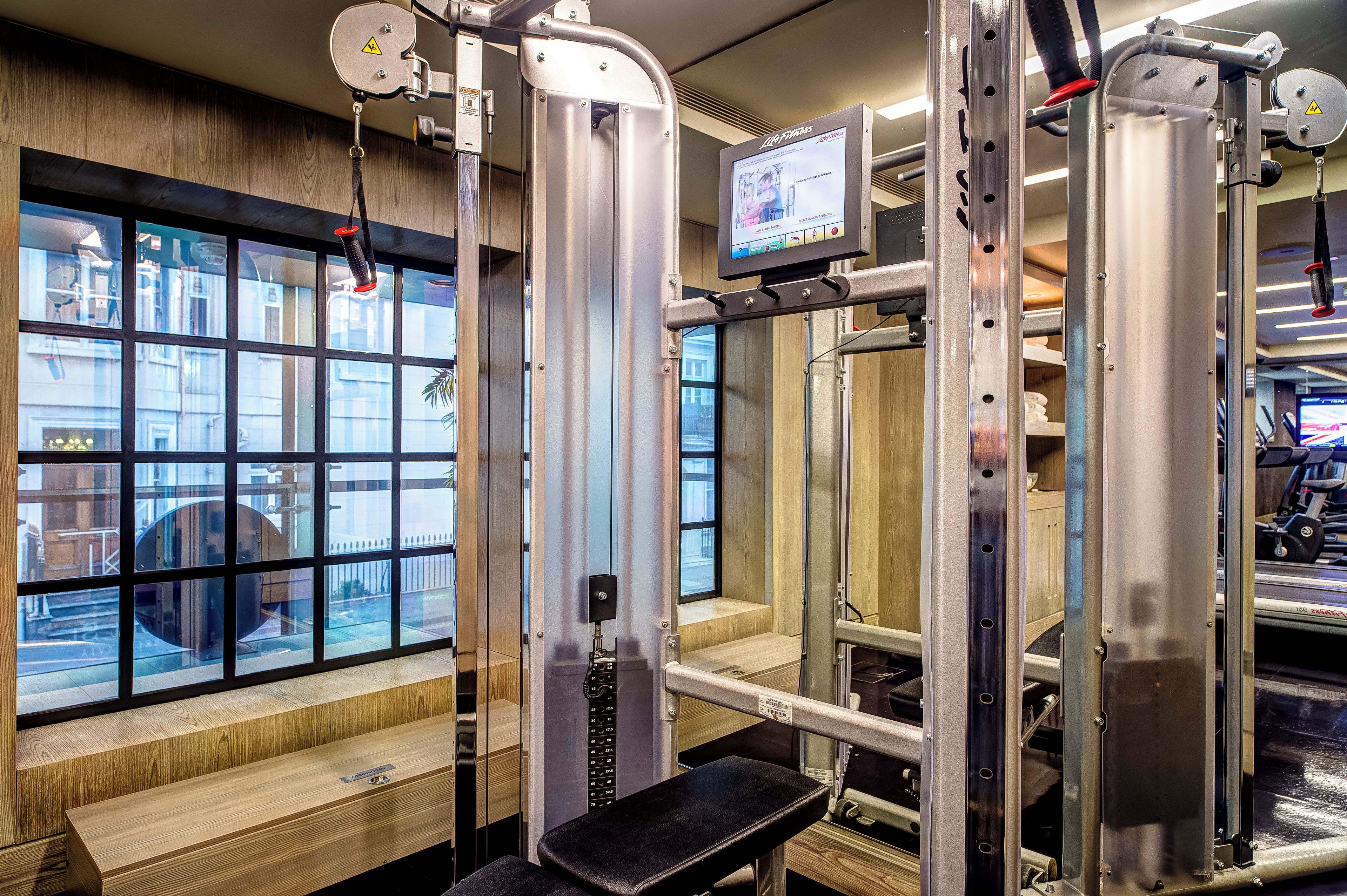 Ein Fitnessraum mit Trainingsgeräten, einem Fernsehbildschirm und einem Fenster mit Blick auf die Straße.