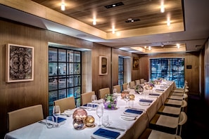 Una larga mesa de comedor dispuesta para un evento formal, con sillas, velas y cristalería.