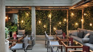 An outdoor seating area with modern furniture and hanging lights, surrounded by a wooden deck and a wall covered in greenery. - The Hari (London)
