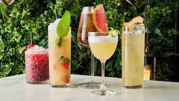 Vier verschiedene Cocktails auf einem Marmortisch mit grüner Blattkulisse.