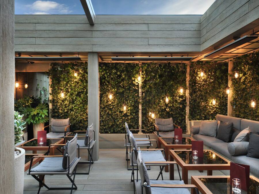 Een terras met tafels en stoelen, een houten vlonder en een muur begroeid met groen.