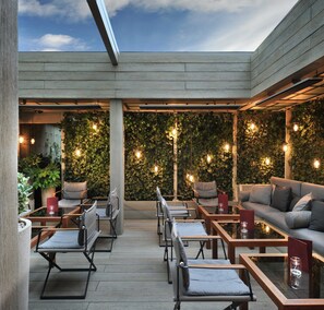 Un espacio al aire libre con mesas y sillas, una terraza de madera y una pared cubierta de vegetación.