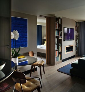 Una sala de estar moderna con un televisor de pantalla plana, una estantería, un comedor con mesa y sillas, y una obra de arte azul grande en la pared.