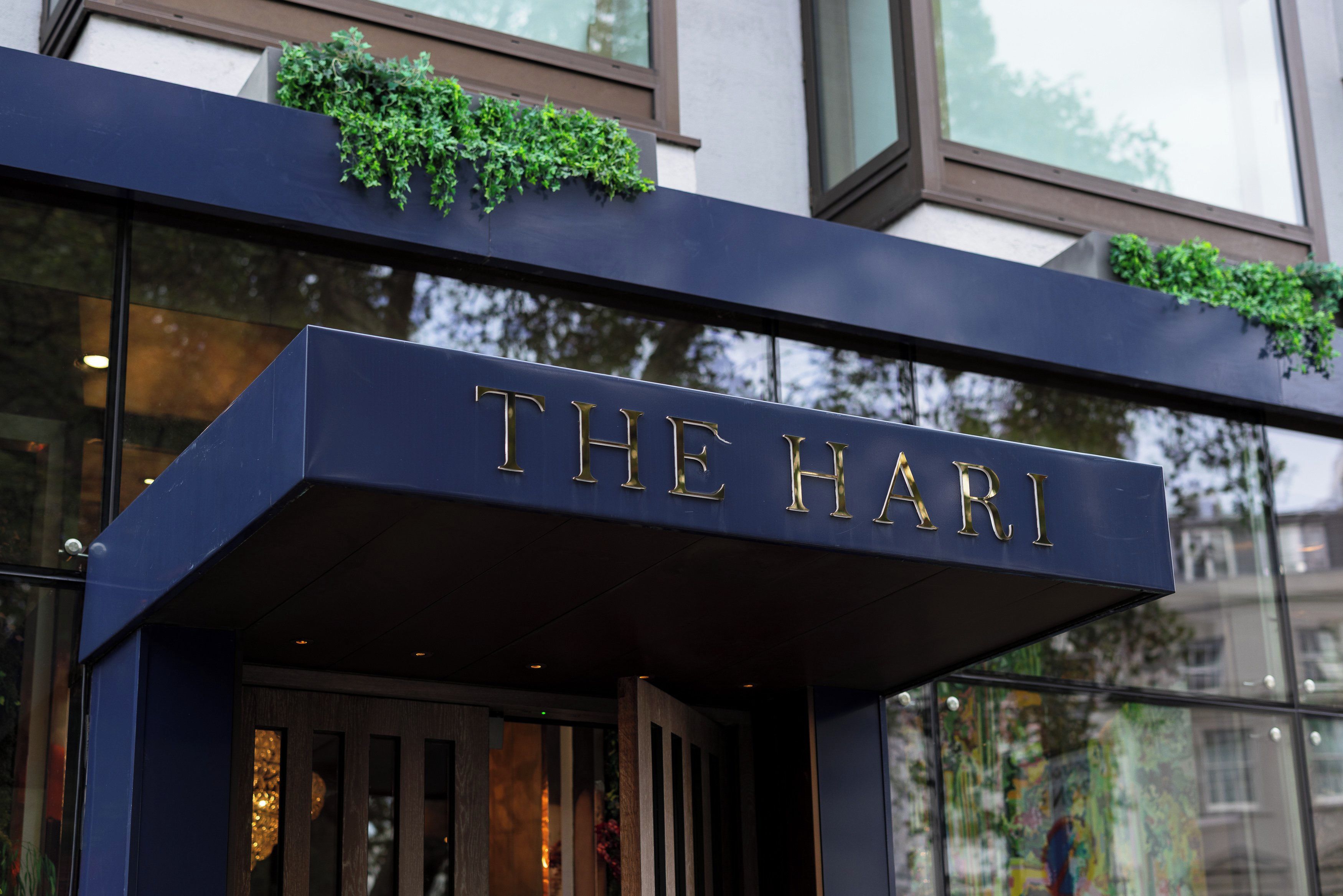 Entrada de edifício com fachada escura e uma placa com a inscrição 'THE HARI'.