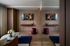 Una habitación de hotel moderna con piso de madera, una mesita de mármol, un jarrón con flores y dos taburetes rojos.