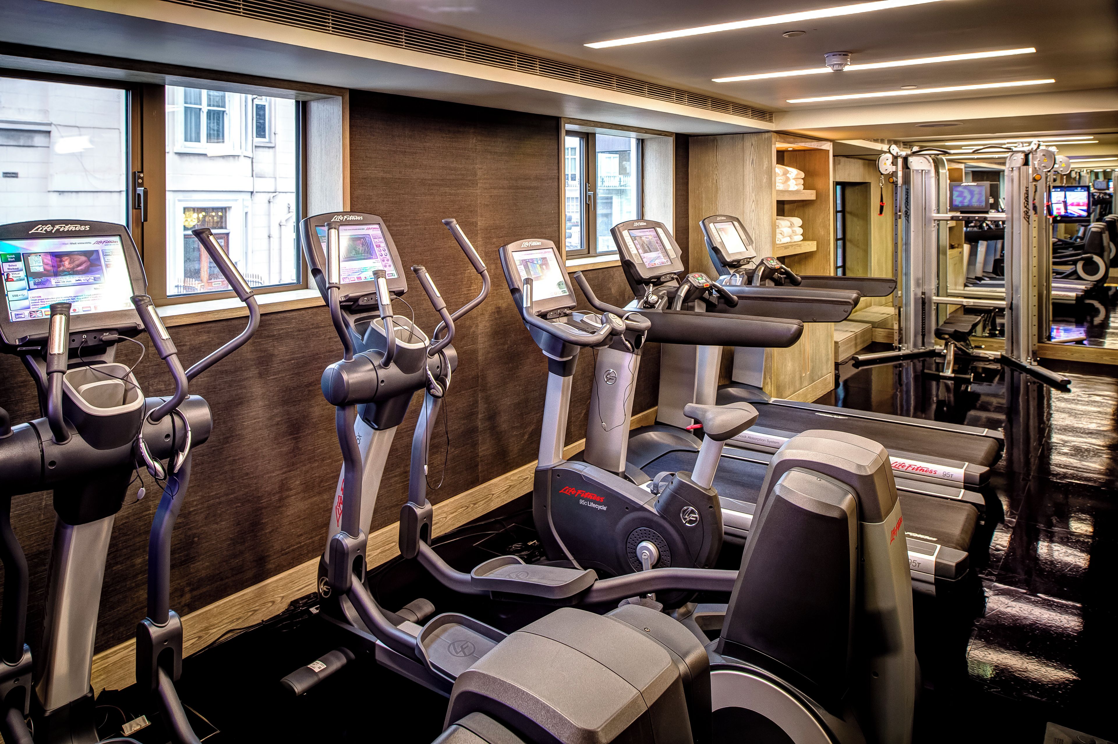 A gym with multiple cardio machines, including treadmills and elliptical trainers, with digital screens and control panels.