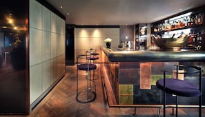 Zona de bar moderna con mostrador, taburetes y una amplia selección de licores.