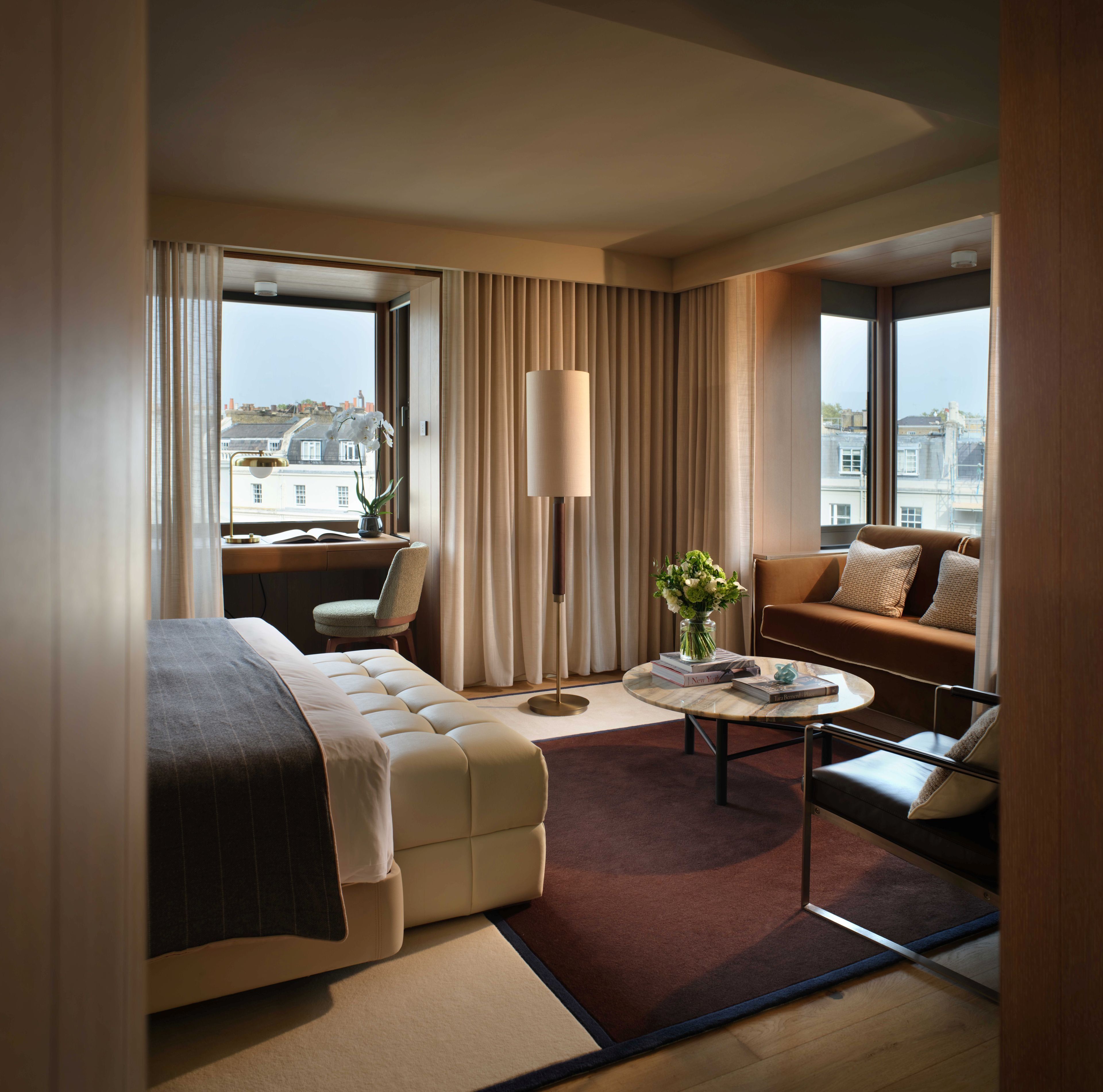 Een hotelkamer met een bed, een bank, een bureau met een stoel, een lamp en uitzicht op gebouwen.