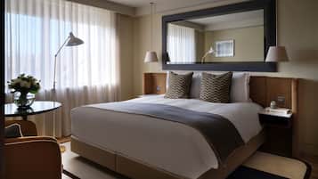 A hotel room with a large bed, bedside lamps, a round table with a vase of flowers, and a chair.