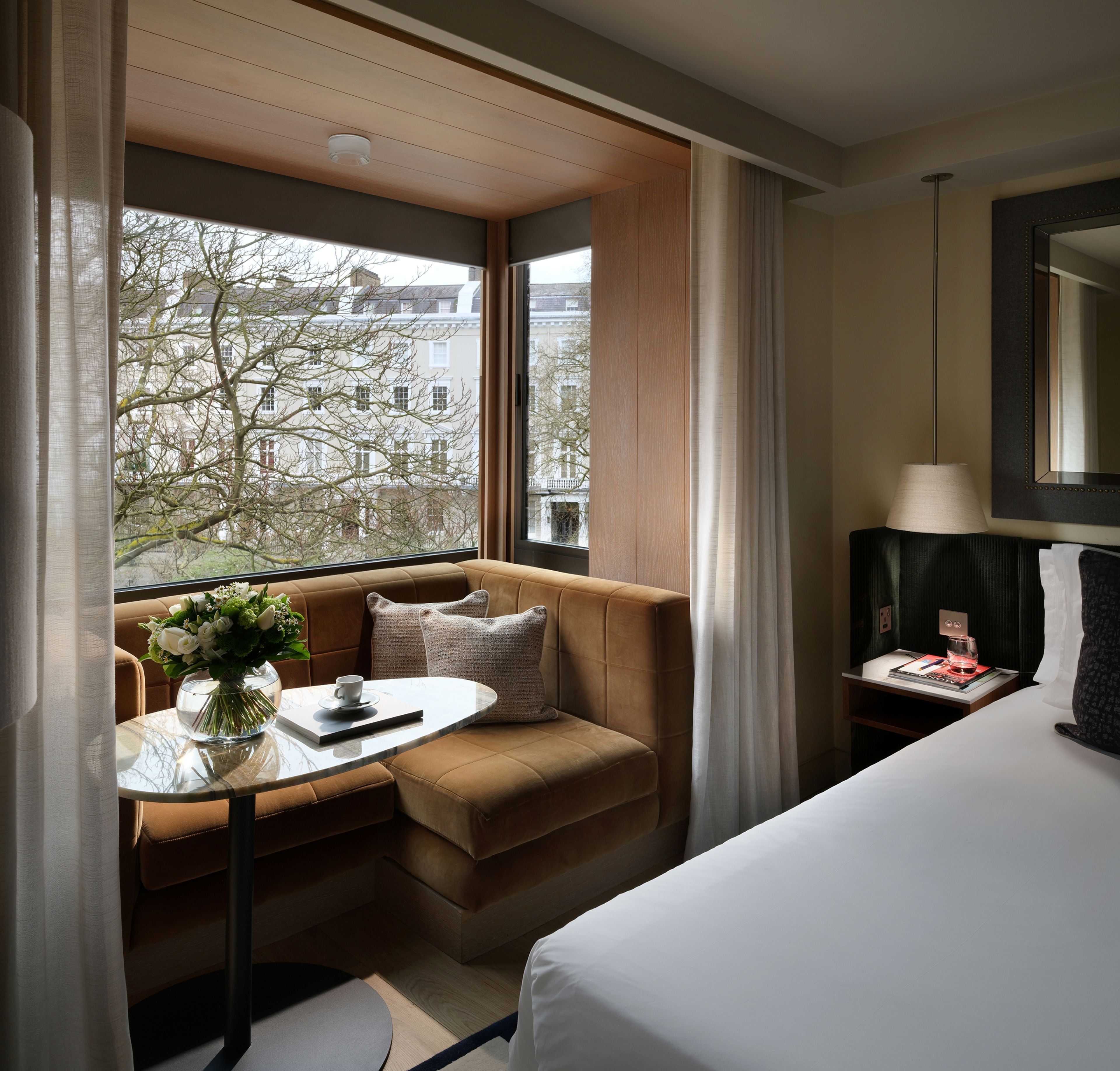 Quarto de hotel com cama, sofá, pequena mesa com um vaso de flores e lumin ária.