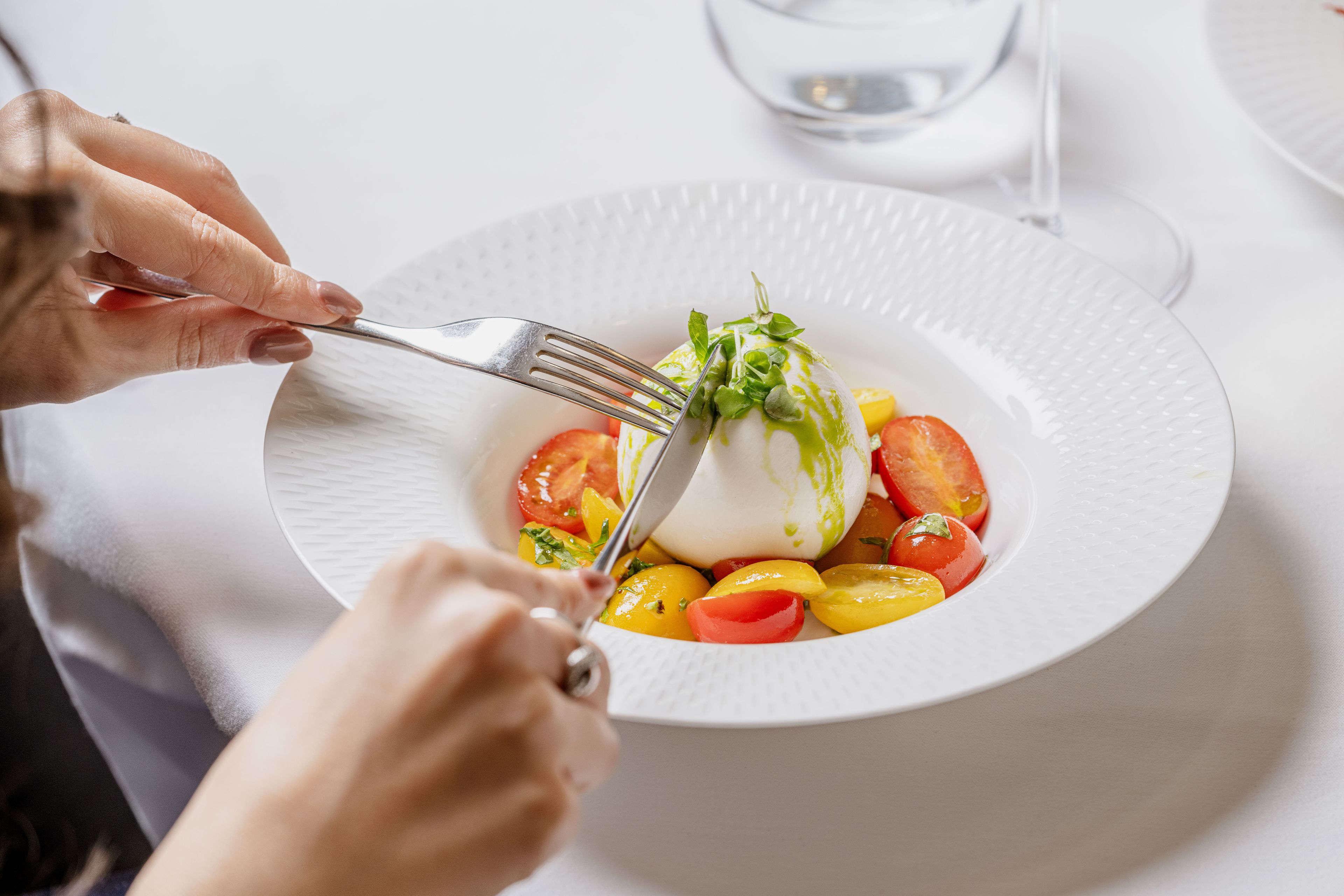 A person cutting a salad with a fork on a white plate.