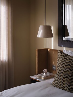 Habitación de hotel con cama, mesita de noche con lámpara, almohada estampada y espejo en la pared.