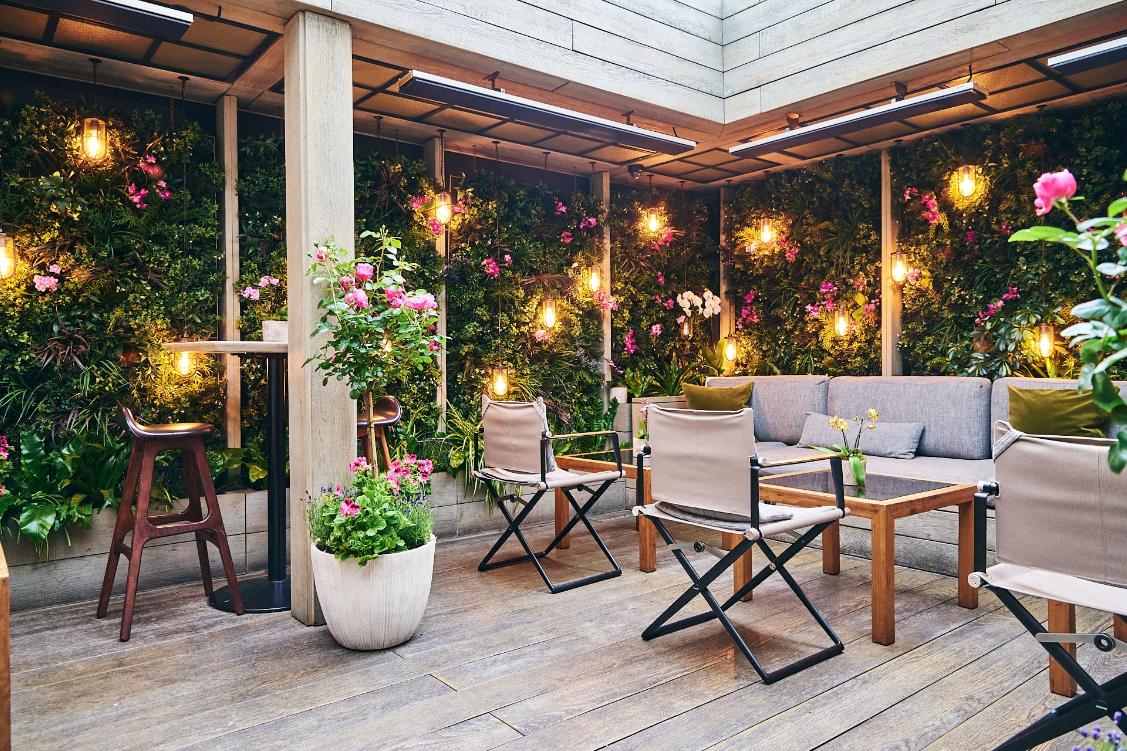 An outdoor seating area with wooden flooring, cushioned seating, and hanging lights.