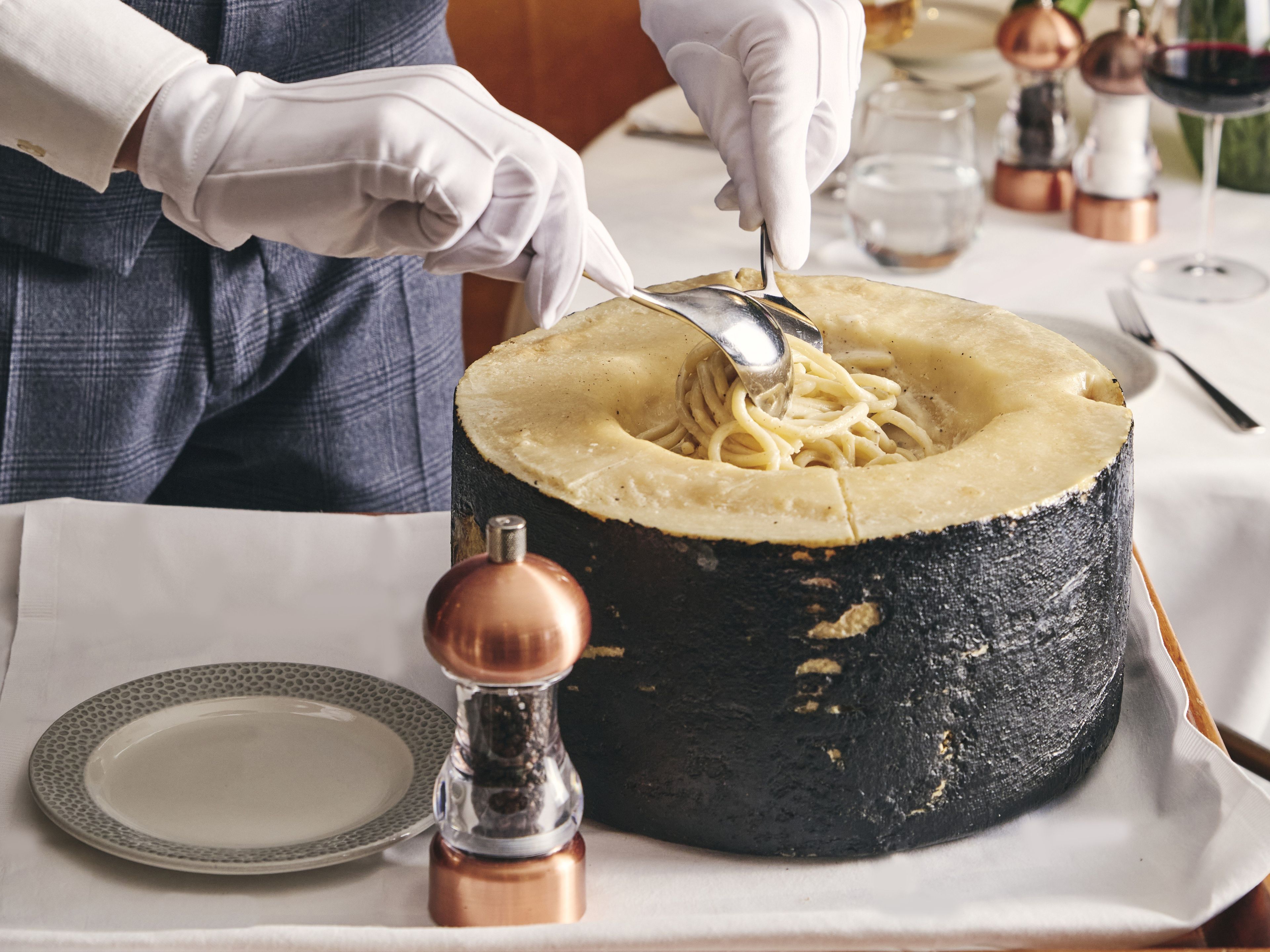 Eine Person serviert Pasta aus einer großen, runden, schwarzen Keramikschale.