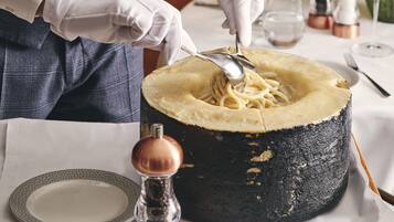 Eine Person serviert Pasta aus einer großen, runden, schwarzen Keramikschale.