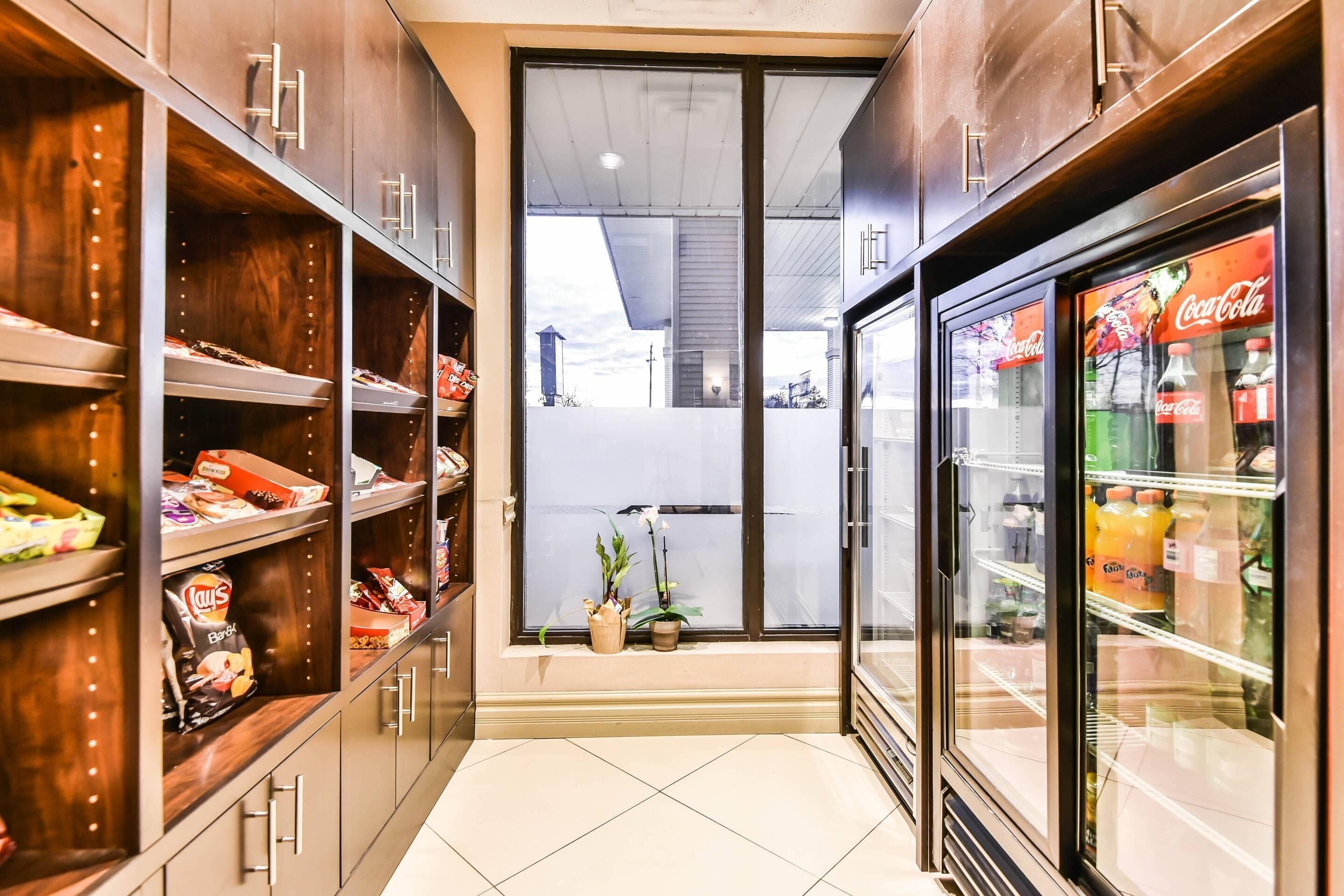 A corridor with wooden cabinets, a Coca-Cola refrigerator, and a window with a view of the outside.