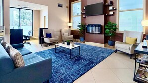 Un salón amplio con alfombra azul, dos sillones, un sofá, una mesa de centro y un televisor de pantalla plana montado en la pared.