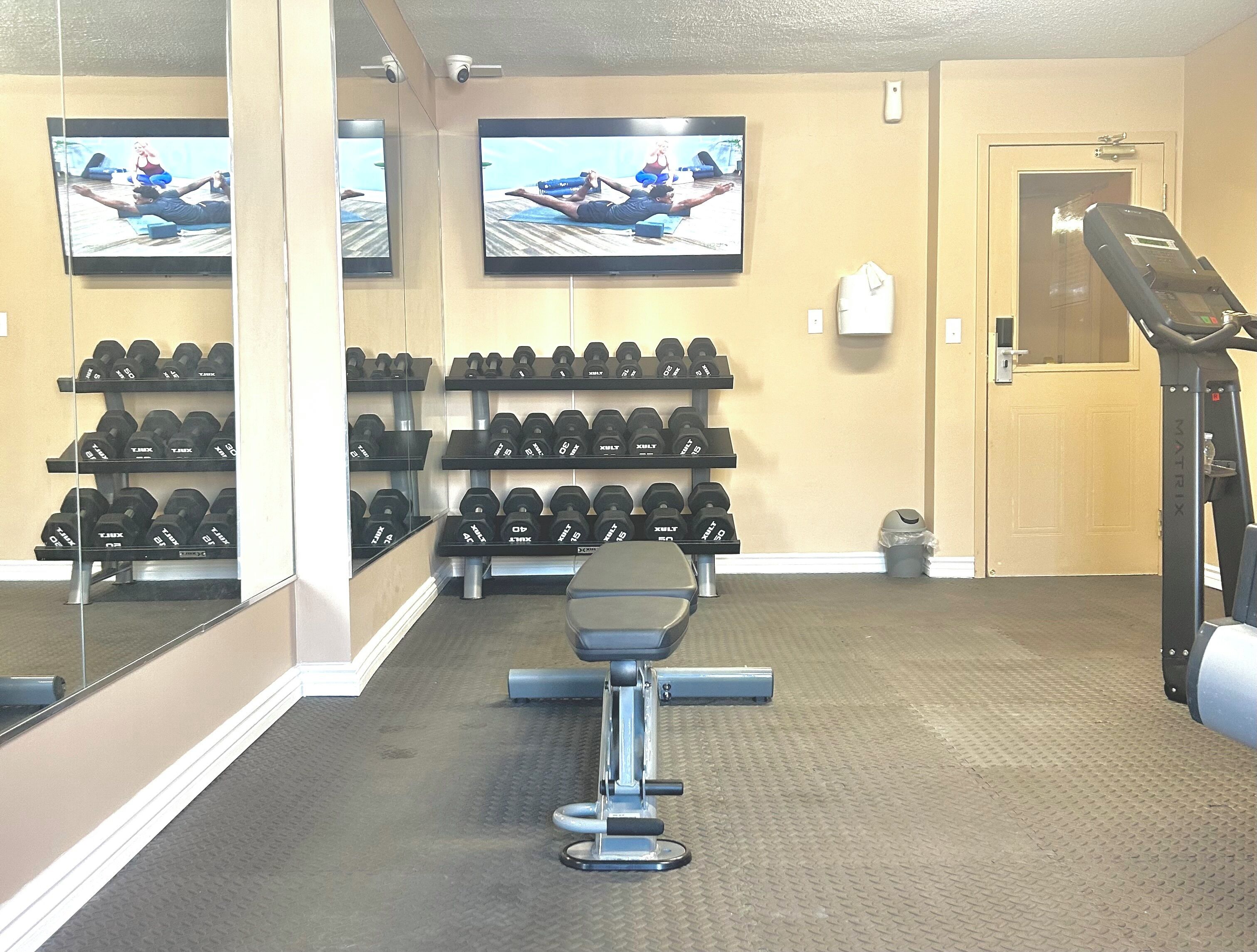 Un gimnasio con equipamiento de ejercicio, pesas y una cinta de correr.