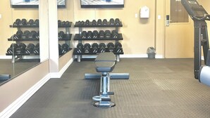 Un gimnasio con equipamiento de ejercicio, pesas y una cinta de correr.