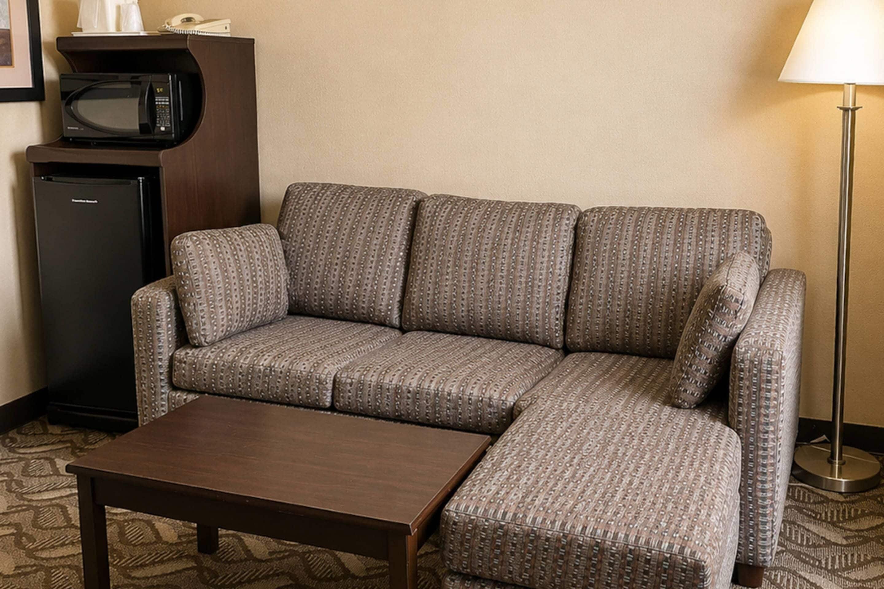 A hotel room with a sofa, a small table, a microwave, and a lamp.