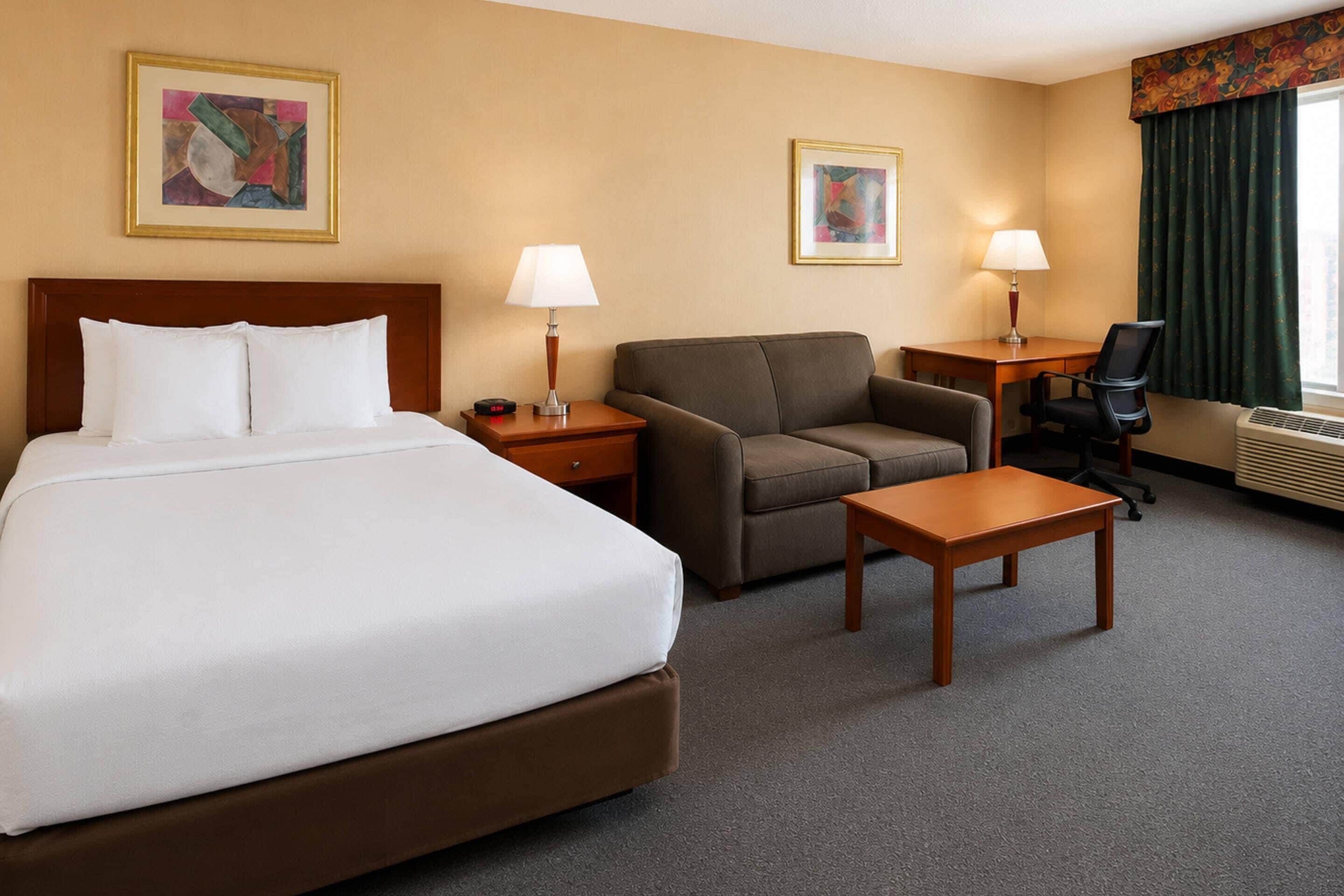 A hotel room with a large bed, a sofa, a small table, a desk, two lamps, and two framed pictures on the walls.