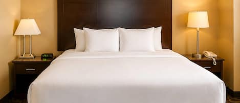 A hotel room with a large bed, two bedside tables, a nightstand, a lamp, and a telephone.