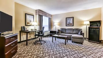 A hotel room with a sofa, a desk with a computer, a television, a lamp, and a microwave.