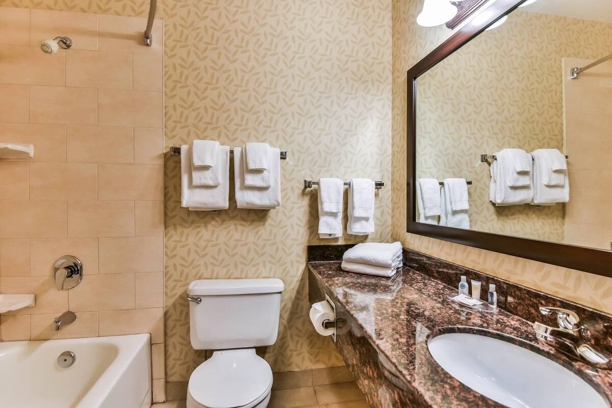 A bathroom with a bathtub, toilet, two sinks, and towels hanging on the wall.