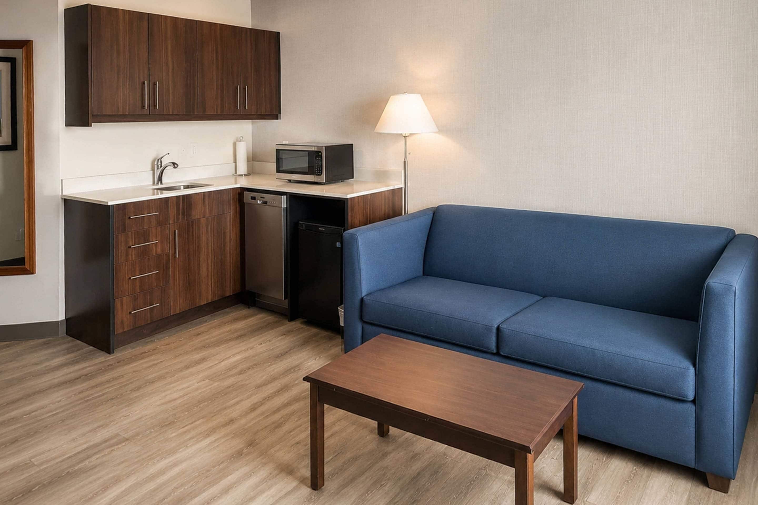 Un espacio habitable compacto con kitchenette, un sofá azul y una mesa de madera.