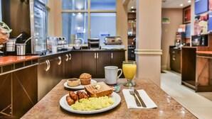 Una mesa de desayuno con tostadas, muffins, salchichas y huevos revueltos.