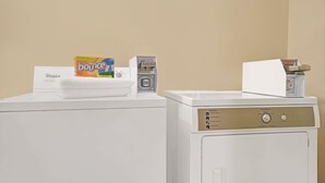 Une machine à laver à chargement frontal, dotée d’un panneau de commande, d’une boîte de lessive Bounce et d’une serviette de la marque Whirlpool posée sur le dessus.