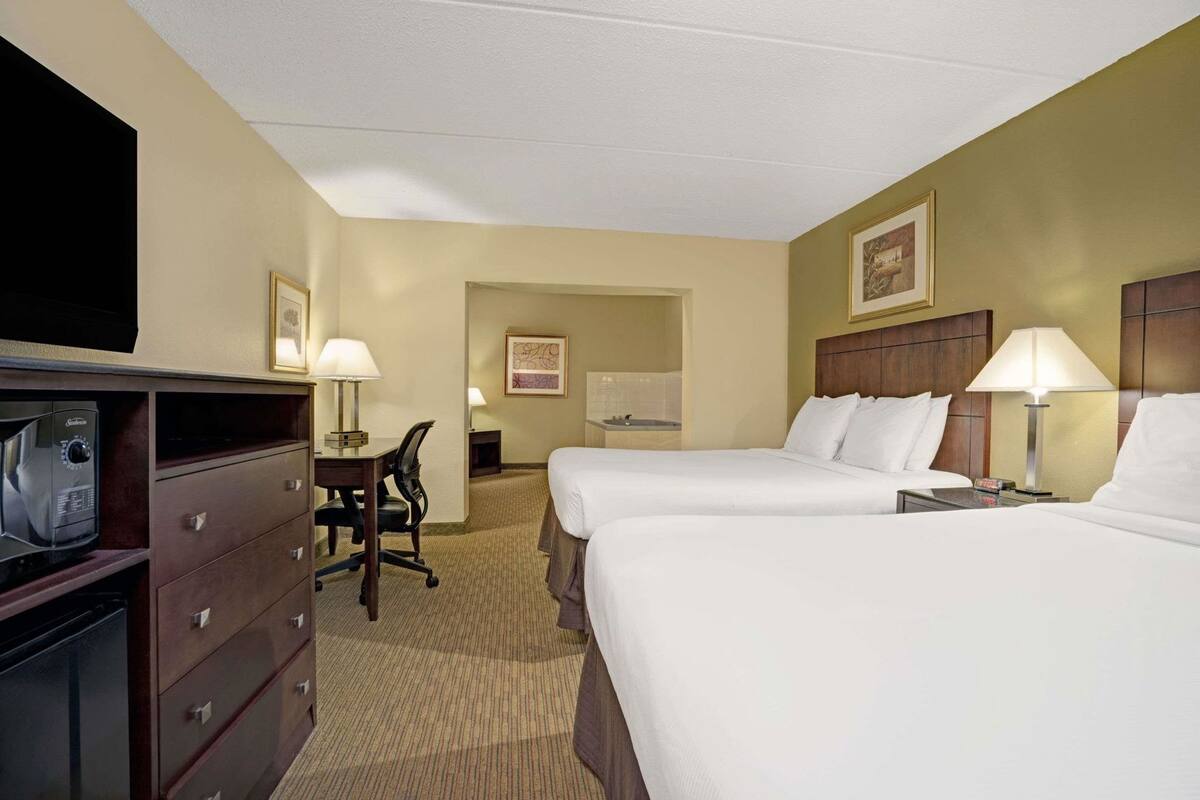 A hotel room with two beds, a desk, a chair, a television, and a minibar.