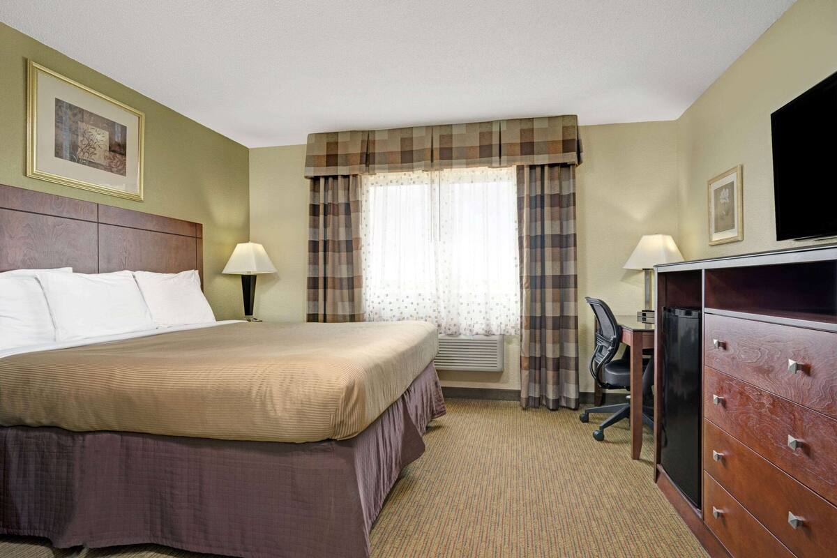A hotel room with a bed, a desk, a chair, a dresser, and a television.