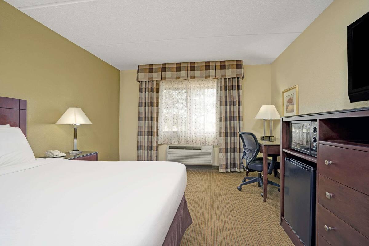 A hotel room with a large bed, a desk with a chair, a television, and a refrigerator.