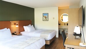 A hotel room with two beds, a desk with a lamp, a mirror, and a wall-mounted light fixture.