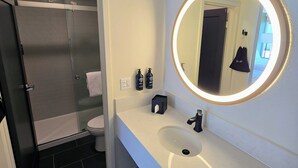 A modern bathroom with a glass shower enclosure, a white sink, and a round mirror with a lighted frame.