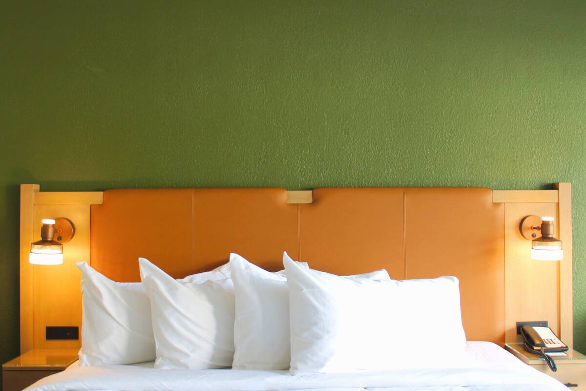 A hotel room with a bed, pillows, a nightstand, a lamp, and a telephone.