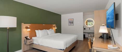 A hotel room with a bed, bedside table, lamp, and a desk with a chair.